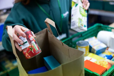 Hands of a volunteer placing a tin of tomatoes into a food parcel