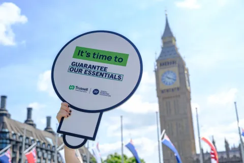 Sign saying "It's time to Guarantee our Essentials" in front of Parliament