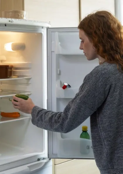 Woman taking an item out of an almost-empty fridge