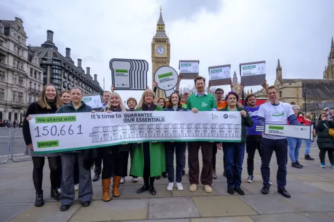 Trussell Trust CEO Emma Revie, actor Charlotte Richie and representatives from food banks stand outside parliament. They are holding a banner that says 'We stand with 150,661 people. It's time to guarantee our essentials'.